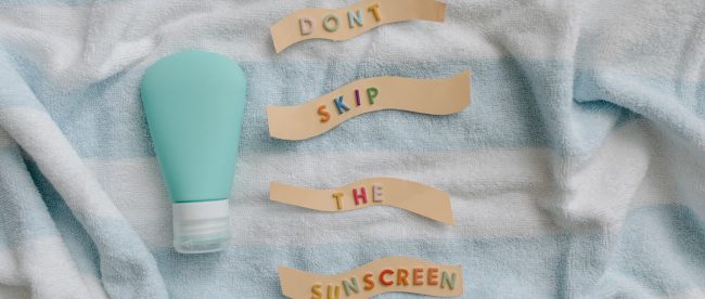 White and blue towel with Don't skip the suncream' sign. Article on Silver Magazine www.silvermagazine.co.uk A striped towel with a bottle of suncream and a sign saying 'Don't skip the sunscreen' on it