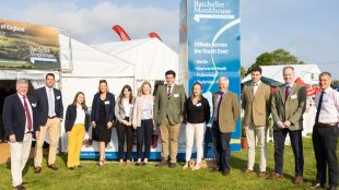 Large group of people stood outside on grass with white tent in the background.