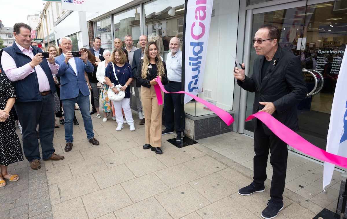 Someone cutting a pink ribbon outside the Guild Care store.