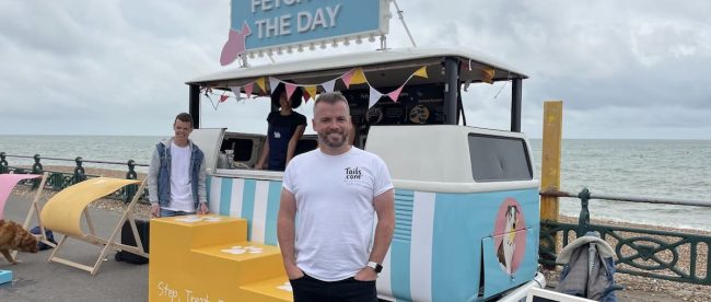 A man standing in front of a dog food truck with sign 'Fetch of the Day' above