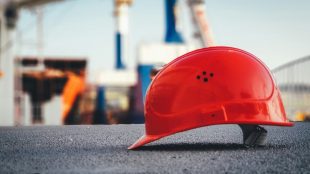 A red hard hat helmet sits on concrete with the sky and poles blurred behind it. Efficiency in construction tips on Title Sussex.
