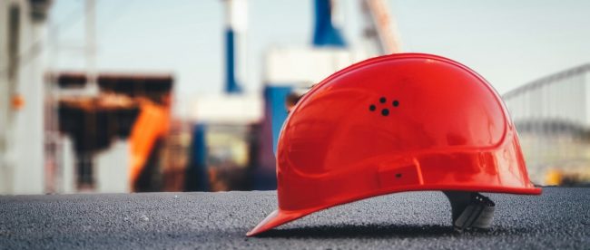 A red hard hat helmet sits on concrete with the sky and poles blurred behind it. Efficiency in construction tips on Title Sussex.