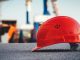 A red hard hat helmet sits on concrete with the sky and poles blurred behind it. Efficiency in construction tips on Title Sussex.
