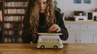 Image shows a young person putting money into a VW camper piggy bank