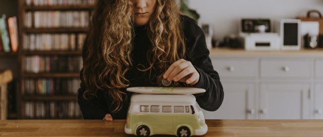 Image shows a young person putting money into a VW camper piggy bank