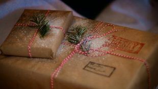 A stack of brown paper packages with red and white bows and stamps printed on them. Last Christmas posting days UK