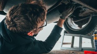 Image shows a man lying on his back working on the underside of the car. It's an anxiety-inducing image