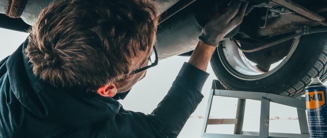 workplace accidents article on Title Sussex Magazine www.titlesussex.co.uk Image shows a man lying on his back working on the underside of the car. It's an anxiety-inducing image