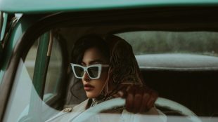 Image shows woman in dark glasses at wheel of car