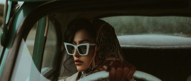 Image shows woman in dark glasses at wheel of car
