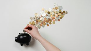 money spread all over surface coming out of a piggy bank and a hand putting money into the piggy bank
