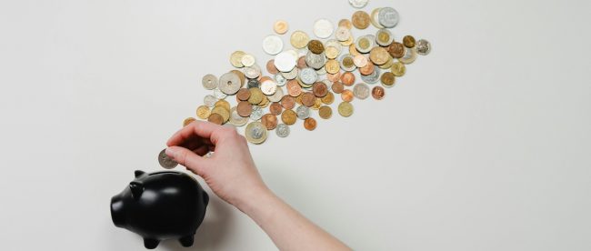money spread all over surface coming out of a piggy bank and a hand putting money into the piggy bank