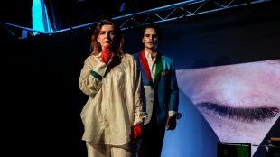 Female actor portraying the George Orwell character Julia, with the male character O'Brian looming towering over her from behind. In the background, a picture of a closed eye representing big brother is projected onto a black background in a tent, which is the theatre. Julia, After 1984 Review, Title Sussex, titlesussex.co.uk