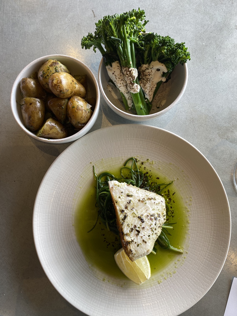Plates of food - new potatoes, broccoli, and a plate of white fish with a green sauce. Rathfinny fish large plate Title Sussex Magazine www.titlesussex.co.uk